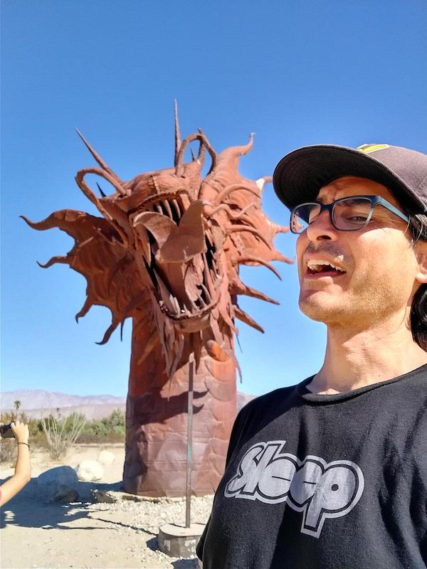 Picture of the author with a metal dragon sculpture in the desert